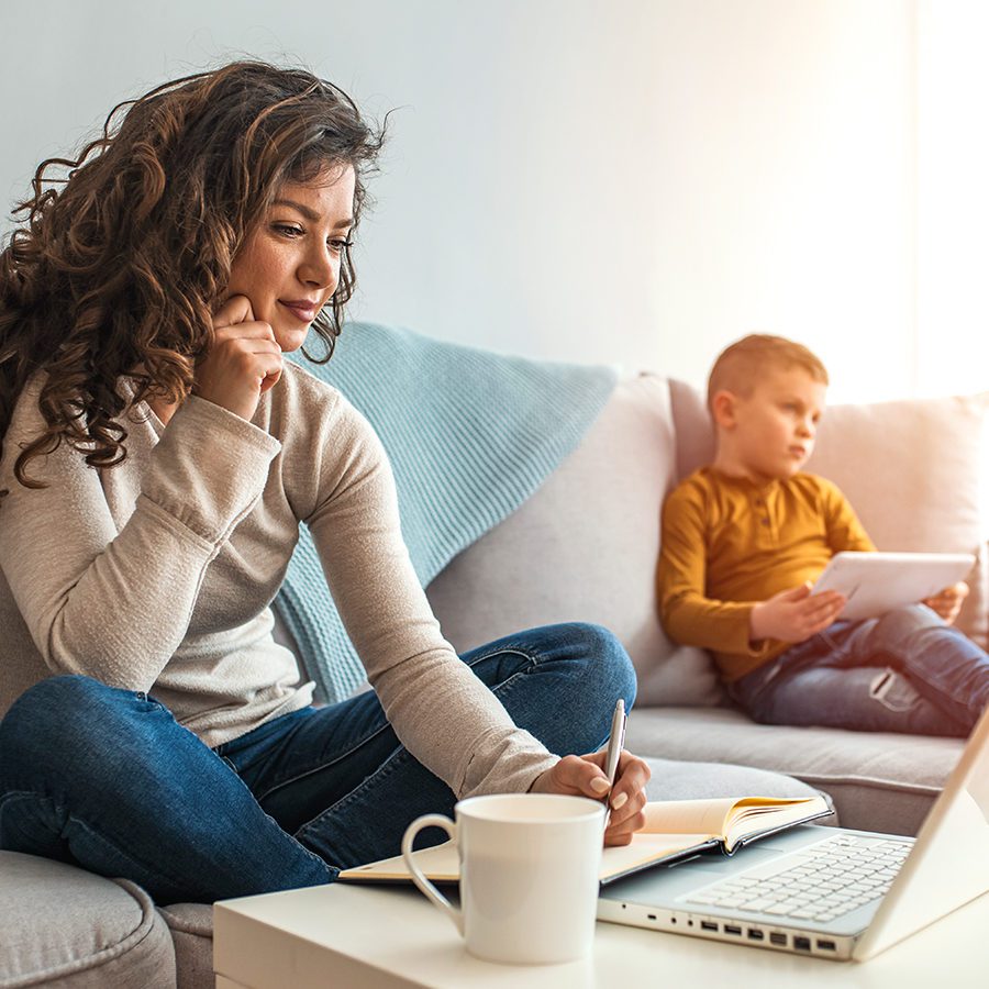 Mother Working on Laptop While Son Plays on Tablet