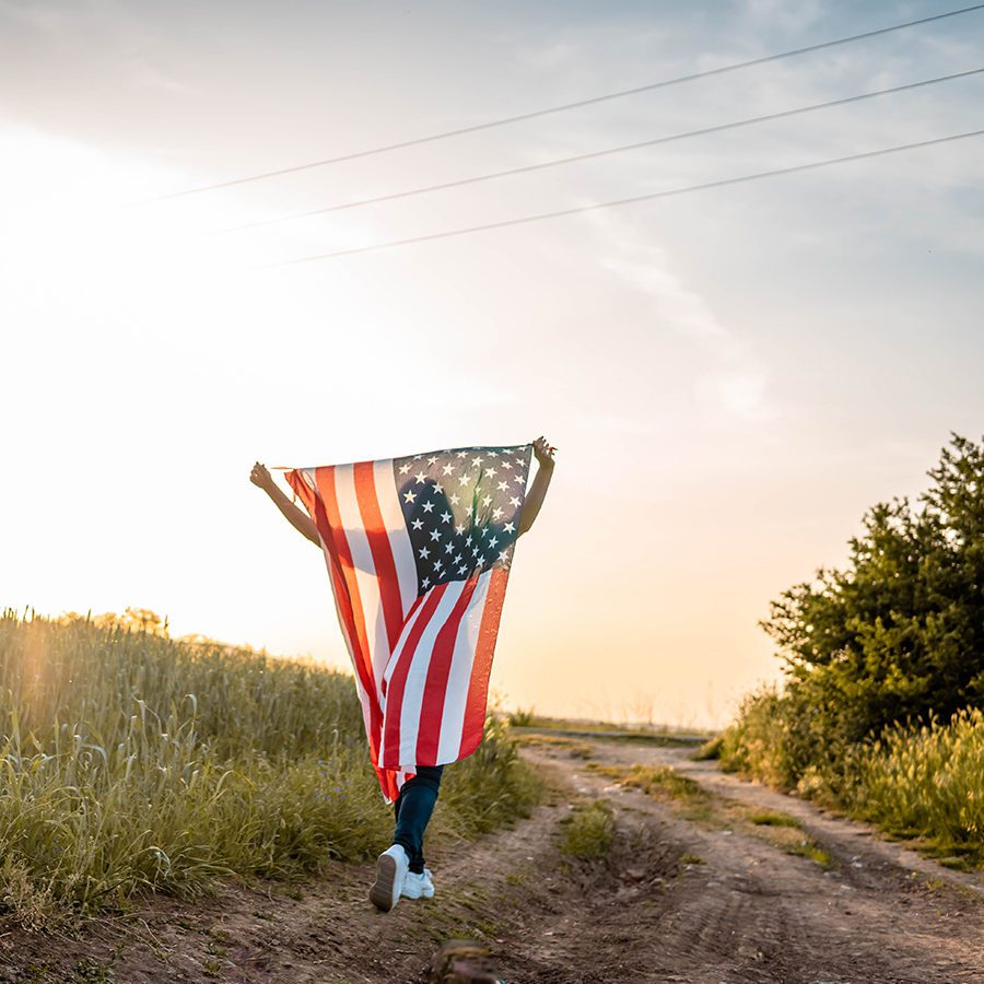 Child Running Down Field Path With Flag