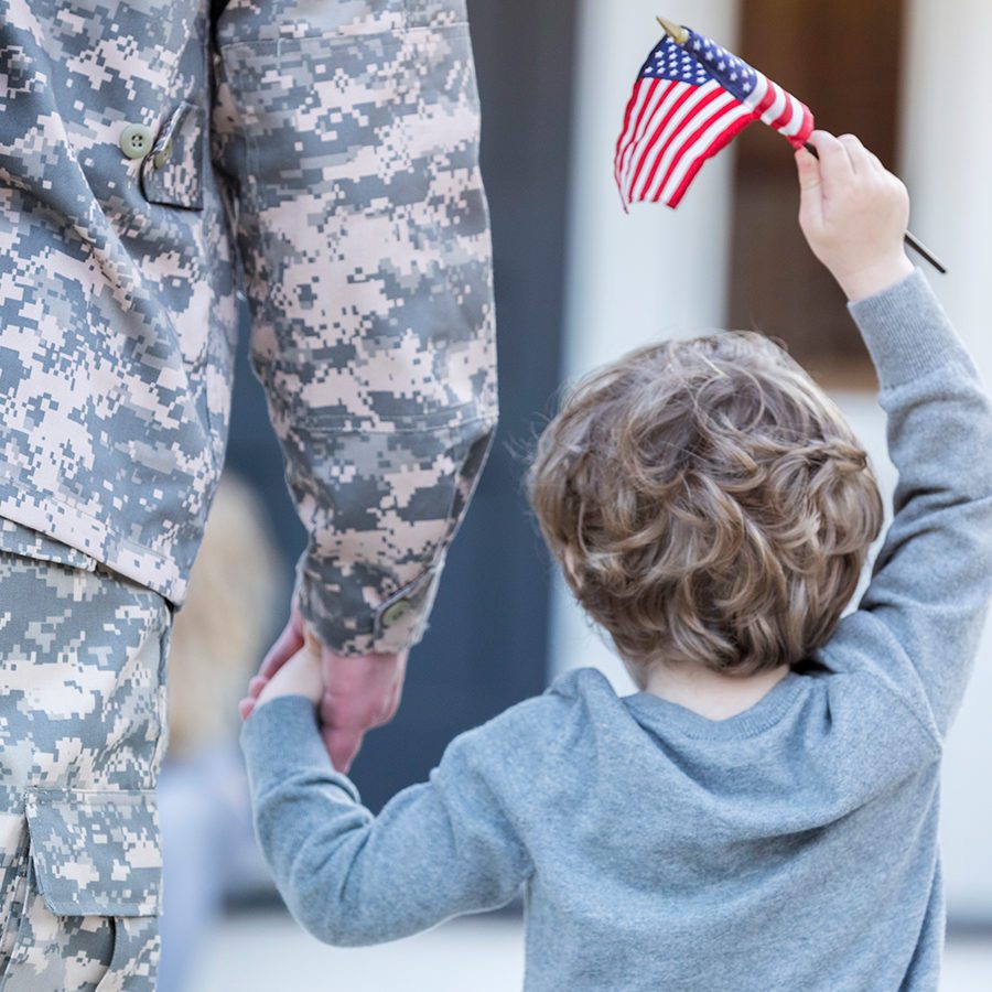 Soldier Holding Son's Hand While Son Waves American Flag