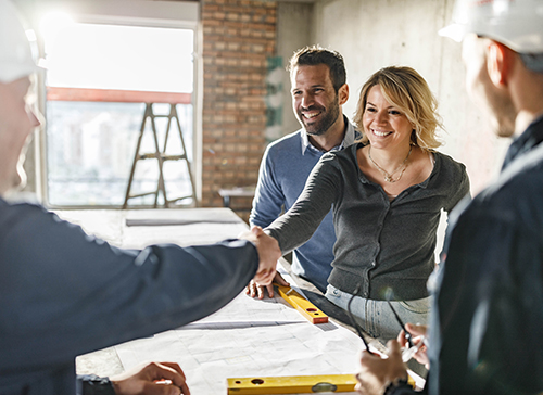 Happy couple gives a handshake to a worker at a construction site