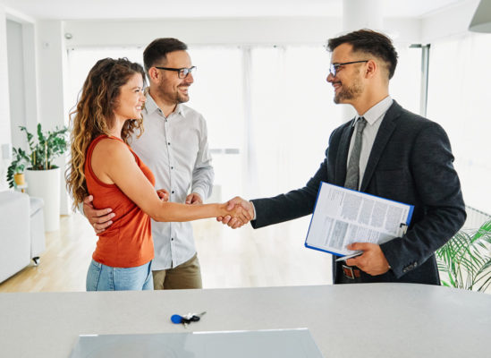 Couple shaking hands with a man who is holding paperwork
