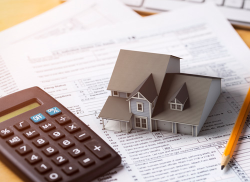 mini house on top of paperwork by the side of a- calculator