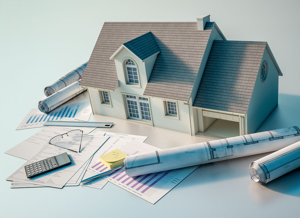 model house on a surface surrounded by reading glasses, construction plans, sticky notes, and calculator