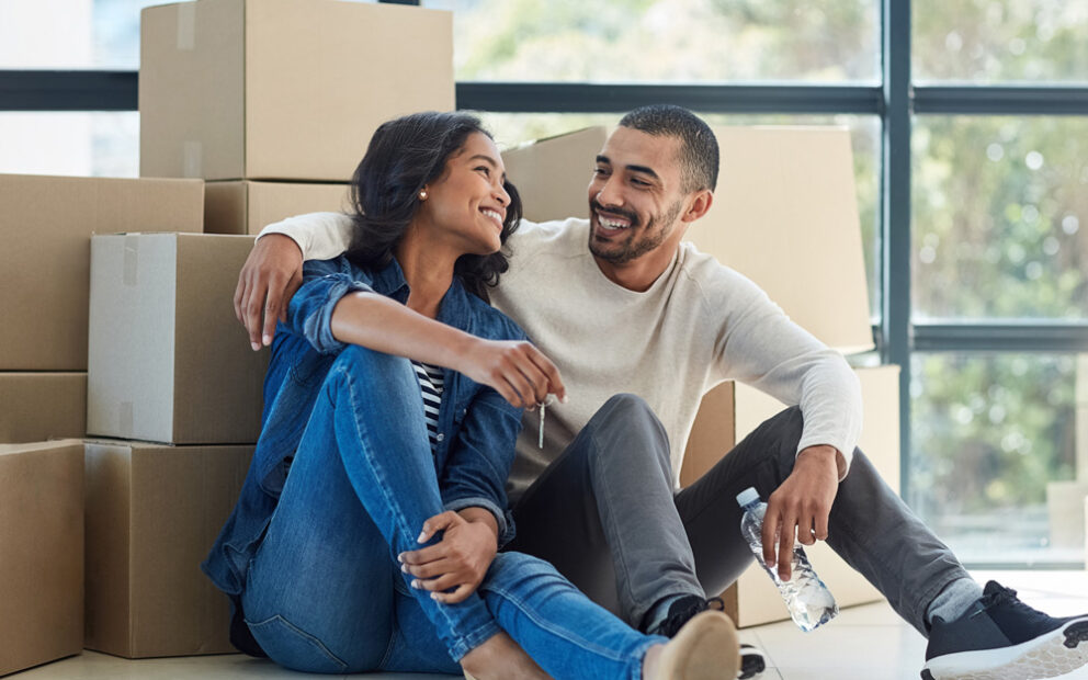 Man and woman smiling at each other while sitting on the floor in front in front of a pile of boxes