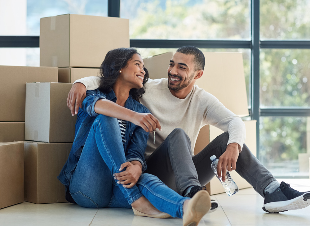 Man and woman smiling at each other while sitting on the floor in front in front of a pile of boxes