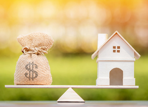 White model house and money bag on a scale