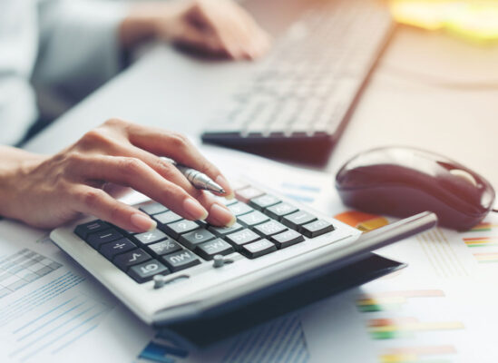 hand holding a pen while using a calculator on a desk where you can see a keyboard and a mouse in the background