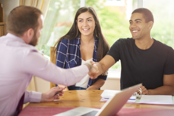 Happy couple shaking hands with businessman, closing a deal.