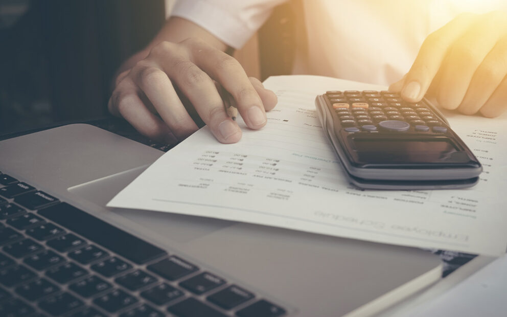 Businessman calculating numbers with calculator and laptop.