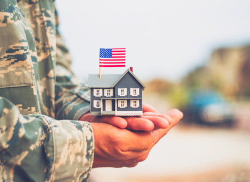 Military Soldier holding a small model home in hands with flag on top.