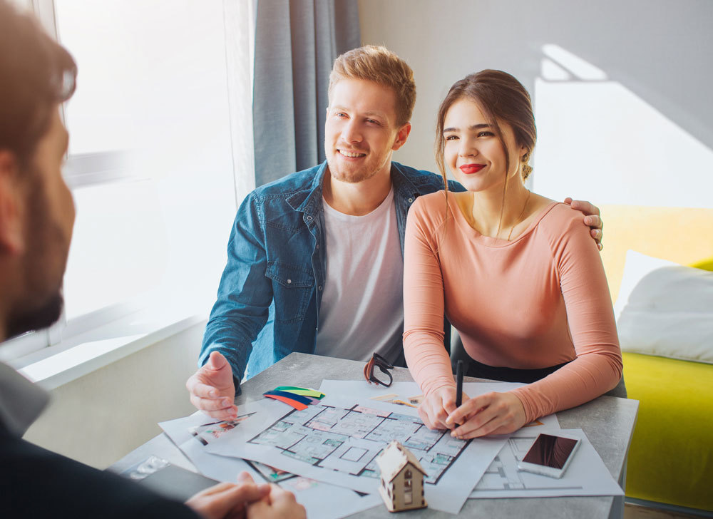 Young couple talking with their developer and looking at blueprints of their future home.