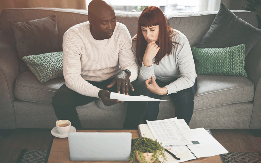 Couple sitting on the couch reviewing their financials with a bit of concern and pondering.
