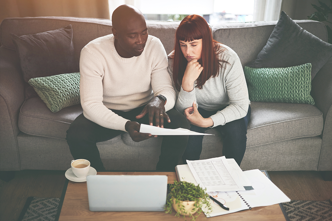 Couple sitting on the couch reviewing their financials with a bit of concern and pondering.