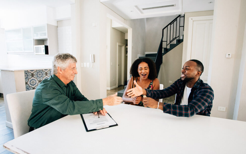 Young couple closing on their new home and shaking hands with their loan officer.