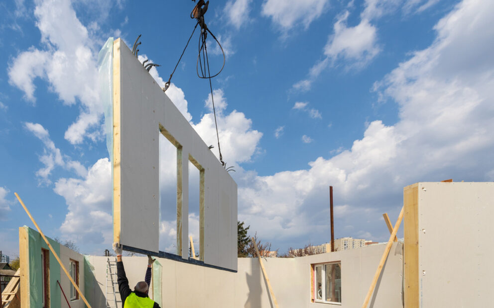Modular home construction site, with builder navigating a piece of the home down to its right spot from a crane.