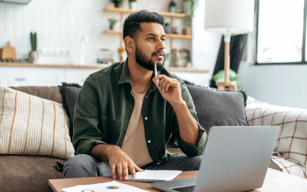 Male sitting on couch, thinking while on his laptop