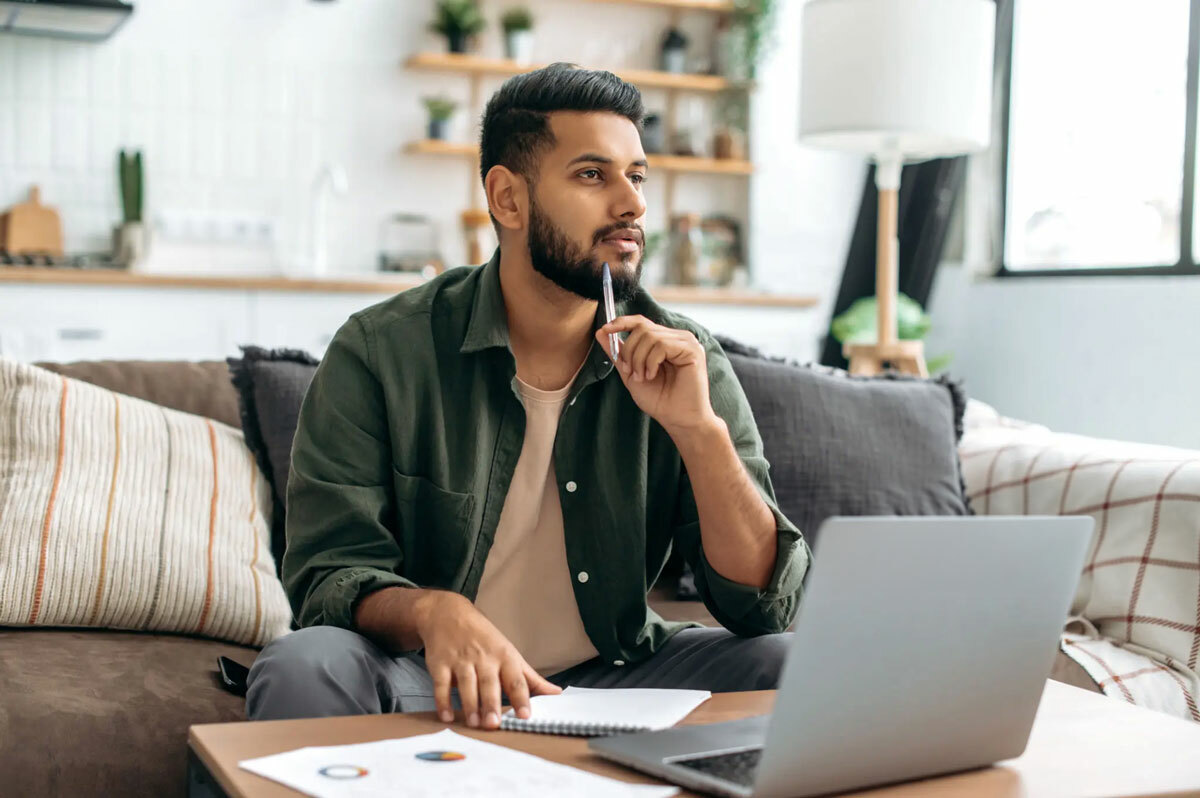 Male sitting on couch, thinking while on his laptop