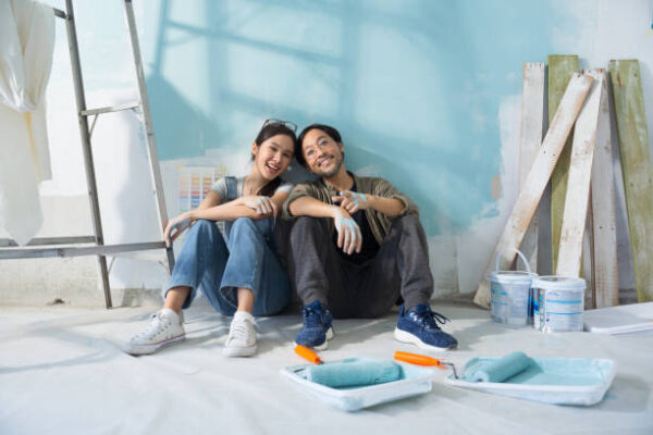 Man and woman sitting down in front of freshly painted wall while smiling