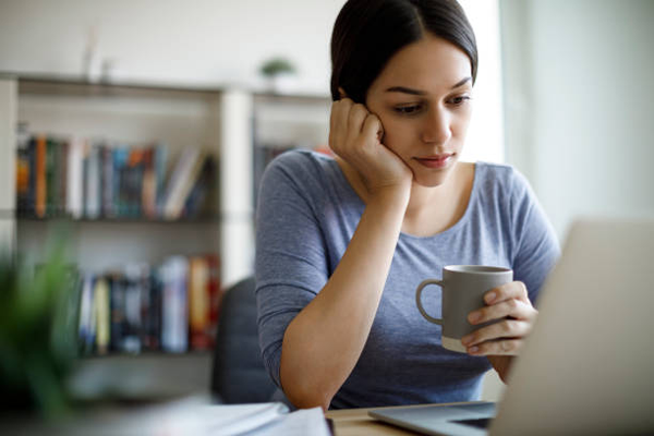 Woman looking over computer screen with cup of coffee in her hand