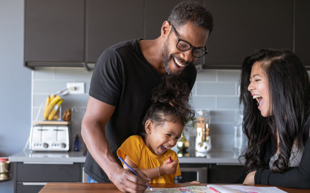 Family of three laughing together in home kitchen