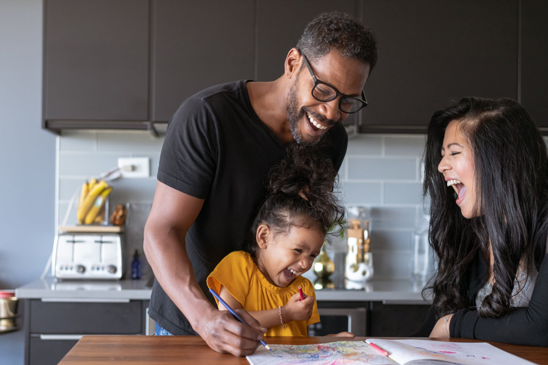 Family of three laughing together in home kitchen