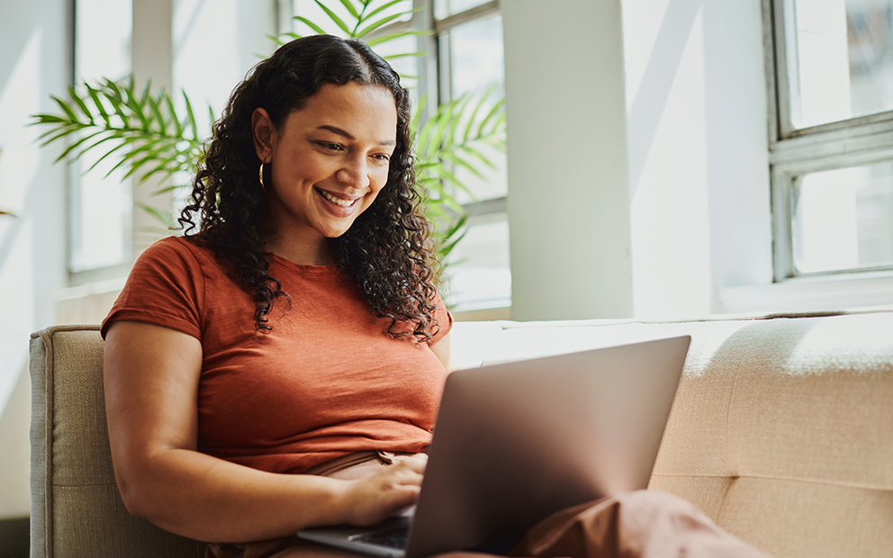 Woman sitting on couch while smiling and looking at her laptop