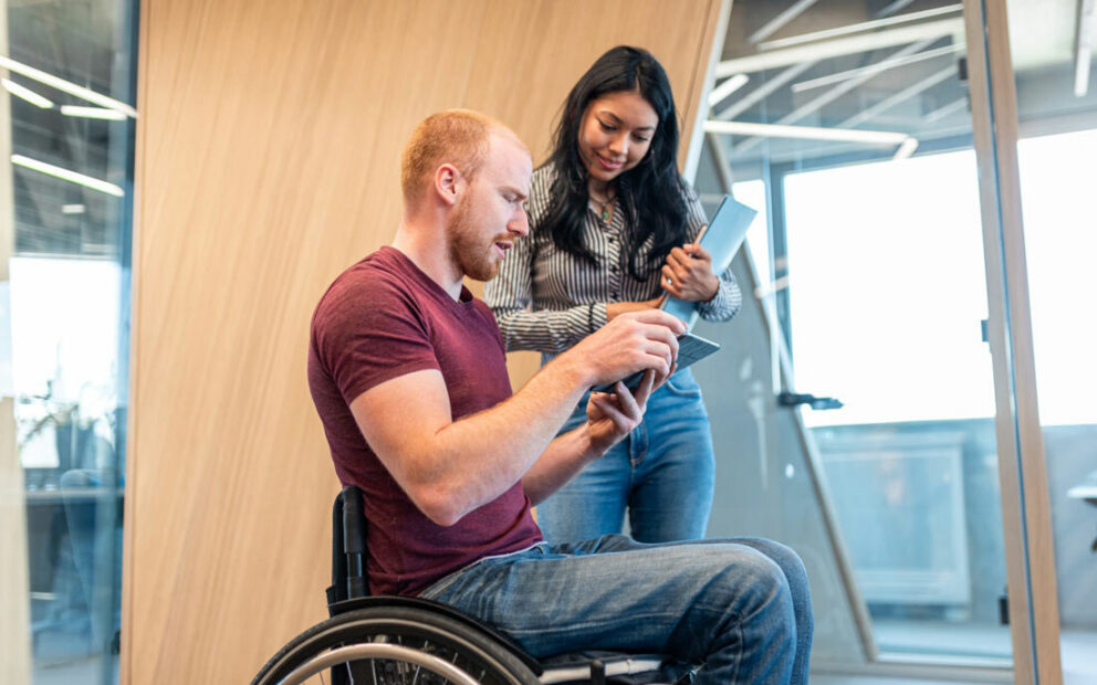 Man in wheelchair looking at document next to woman friend