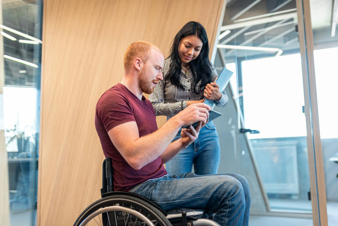 Man in wheelchair looking at document next to woman friend