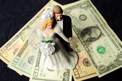 Wedding cake topper on top of dollar bills.