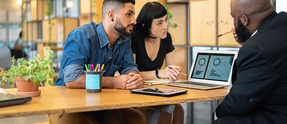 Couple sitting across from loan officer while looking over numbers on computer
