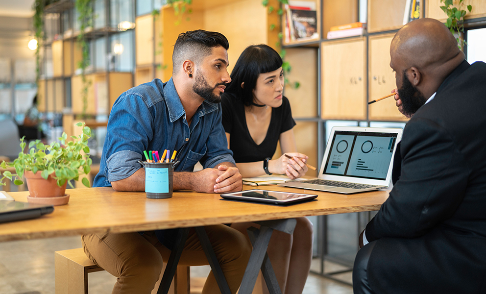 Couple sitting across from loan officer while looking over numbers on computer