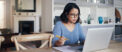 Woman sitting at kitchen table while looking over her notes and laptop
