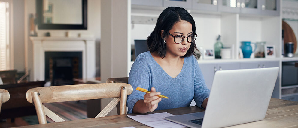 Woman sitting at kitchen table while looking over her notes and laptop
