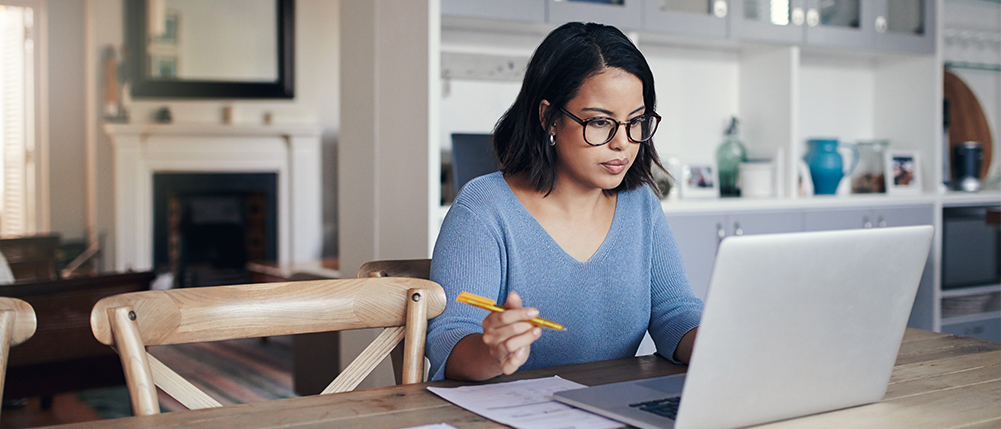Woman sitting at kitchen table while looking over her notes and laptop