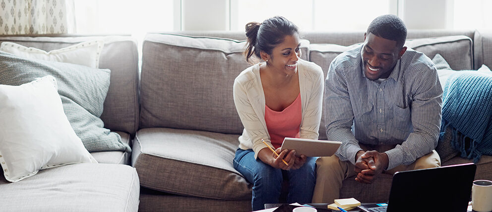 Couple sitting on couch and smiling while discussing over laptop
