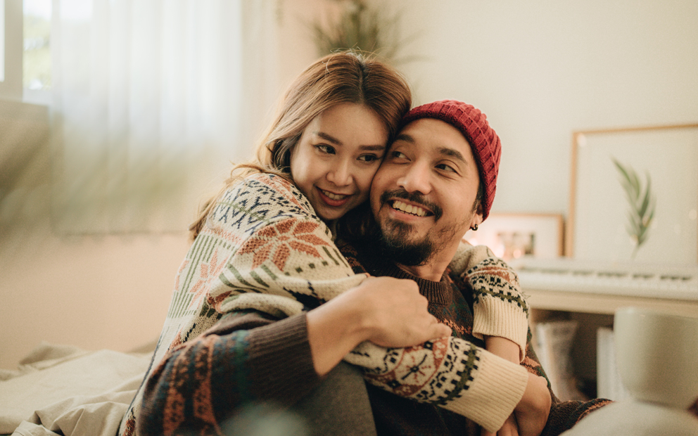 Man and woman couple sitting on floor in living room together while hugging and smiling