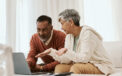 Couple sitting together on couch while they look over and discuss over laptop