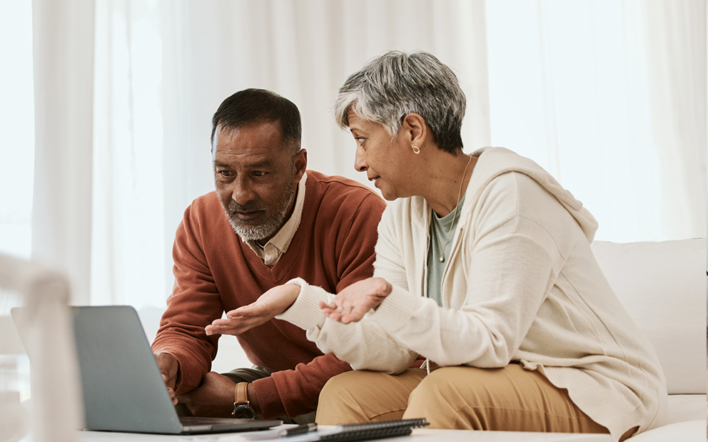 Couple sitting together on couch while they look over and discuss over laptop