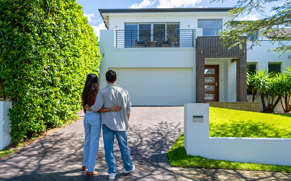 Couple holding each other while they stand at the end of a driveway and look at a house
