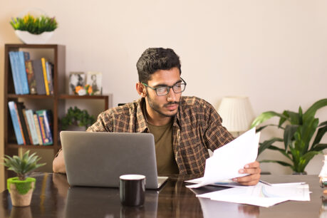 Man sitting at desk while reviewing documents in hand and on laptop