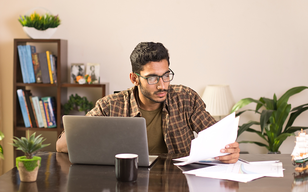 Man sitting at desk while reviewing documents in hand and on laptop