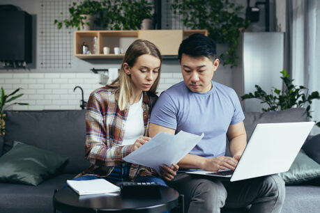 Man and woman couple sitting on couch, discussing documents in hand