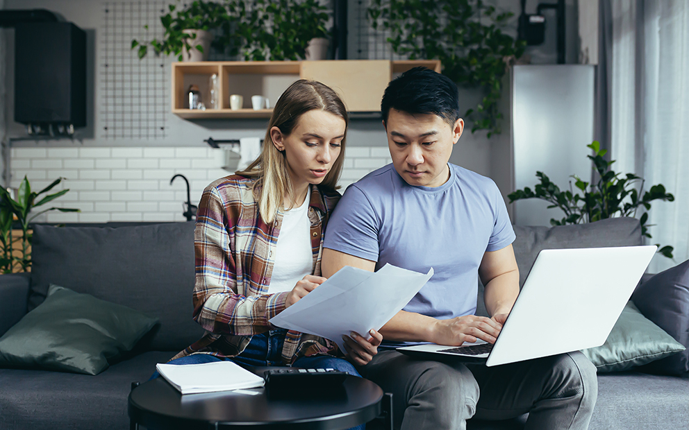 Man and woman couple sitting on couch, discussing documents in hand