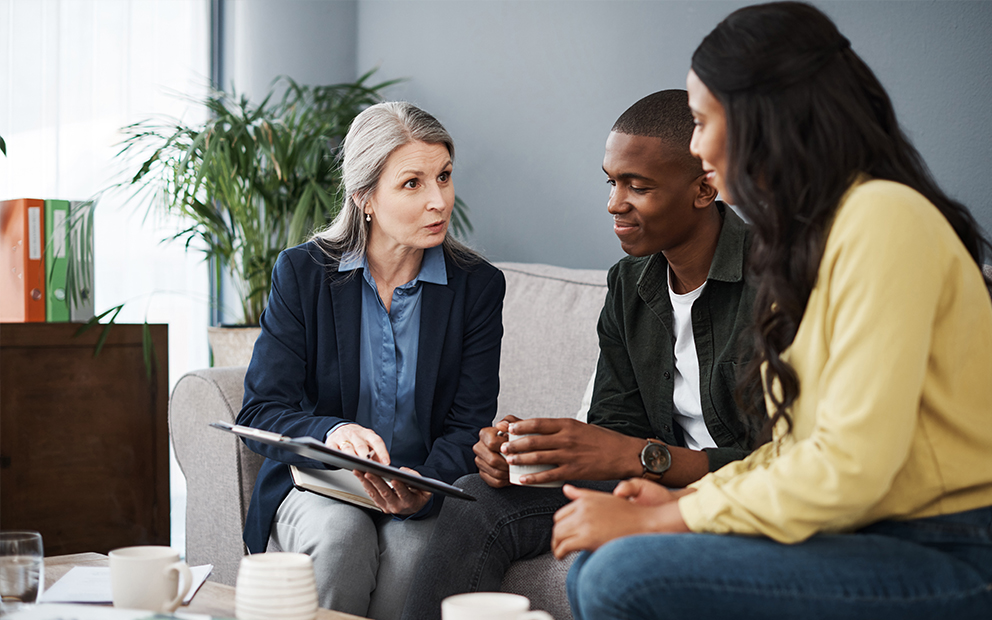 Man and woman couple sitting together on couch as they speak with advisor