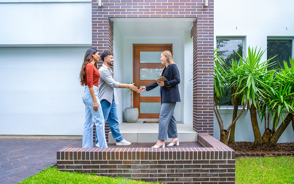 Couple shaking hands with realtor outside of home