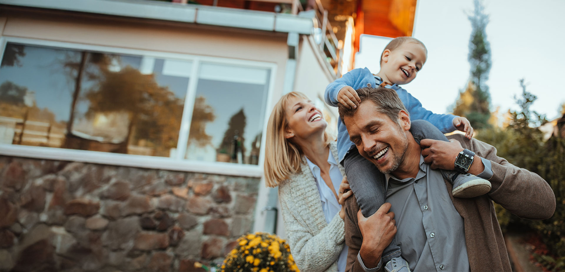 Happy family in front of home kid on dads shoulder