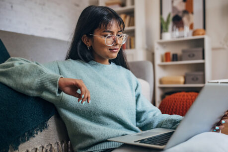 Woman sitting on couch as she reviews info on her laptop