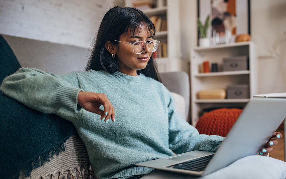 Woman sitting on couch as she reviews info on her laptop