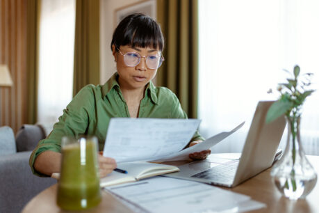 Woman sitting at home desk while comparing financial and digital documents