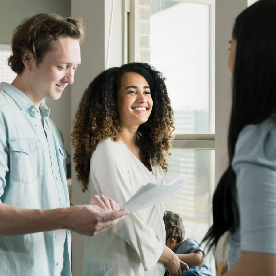 A young woman smiles at a female Real Estate Agent as the woman's husband discusses a real estate contract or lease agreement.